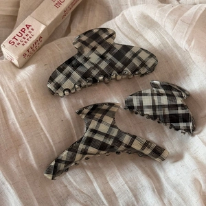 Detailed close-up of three black and white plaid acetate claw clips on beige fabric background
