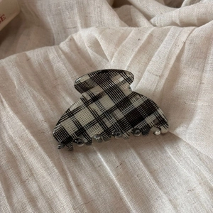 Detailed view of checkered acetate hair claw clip on soft beige linen fabric background
