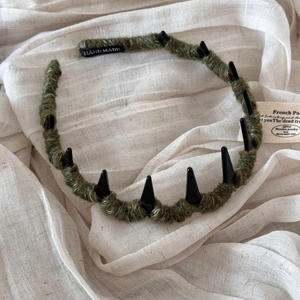 Detail of army green knitted headband featuring black punk spikes and hand made label
