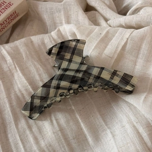 Detailed view of large black and white plaid acetate hair claw clip on soft beige fabric