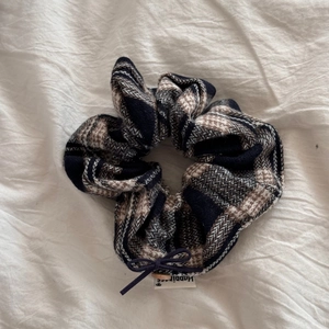 Macro shot of a plaid scrunchie with a dark bow and a Happiness woven label detail