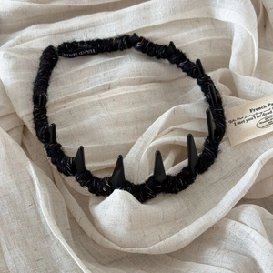 Handmade dark style black yarn headband with pointed horns on soft beige linen background