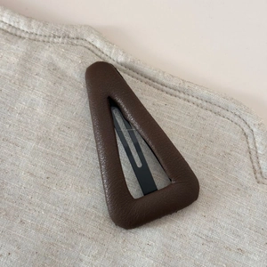 Détail d'une pince à cheveux triangle en cuir marron avec texture litchi et fermoir métallique