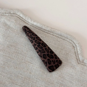 Détail macro d'une pince à cheveux triangulaire léopard sur tissu en lin beige