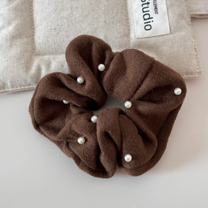 Detail of coffee brown knitted hair scrunchie with white pearls on a soft background