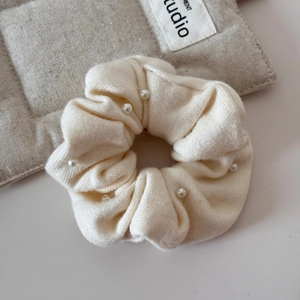 Detail view of a cream knit scrunchie with elegant faux pearl accents and soft fabric texture