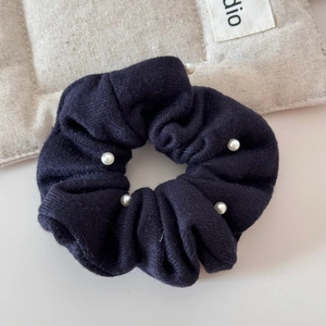 Close-up of navy knit scrunchie with five faux pearls on a rustic linen background