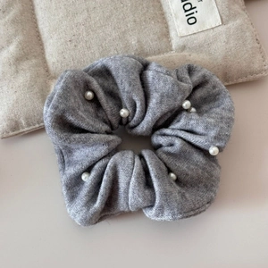 Close-up of a grey knitted scrunchie with white pearl embellishments and soft texture