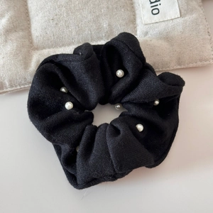 Detailed view of black knitted scrunchie featuring elegant white pearl embellishments