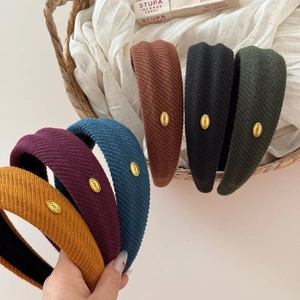 Detail of wide knitted headbands in six colors featuring gold metal logo and rich texture