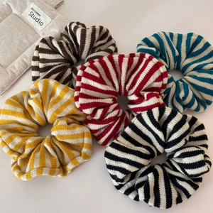 Detail showing five knitted striped oversized scrunchies in various soft warm colors