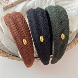 Detail of three knitted wide headbands with gold Korea logo tags in a basket