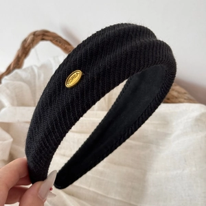 Close-up of black knitted wide headband with gold metal tag and ribbed texture detail