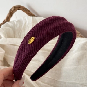 Detail of burgundy knitted wide headband with gold metal tag and ribbed texture detail
