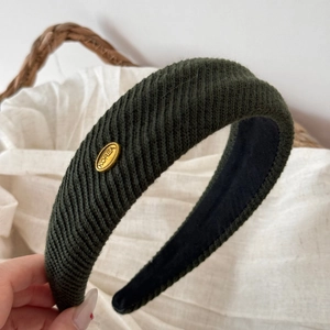 Detail showing dark green ribbed knit fabric texture and gold metal logo on wide headband