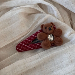 Detailed view of a red plaid hair clip featuring a cute brown flocked bear with a gem
