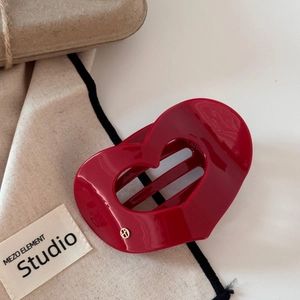 Détail d'une pince à cheveux en cœur rouge en acétate avec un emblème logo doré