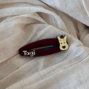 Close-up of a burgundy red velvet hair clip with a cute cartoon bear and white logo detail
