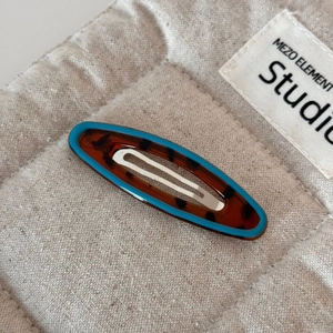 Close-up of tortoise shell hair clip with blue edges on a soft linen textured background