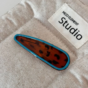 Detail of blue rimmed tortoiseshell hair clip with leopard pattern on textured fabric
