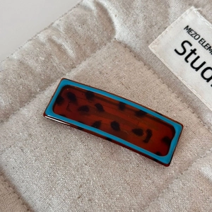 Detail view of a leopard print barrette with a vibrant blue border on a beige fabric base