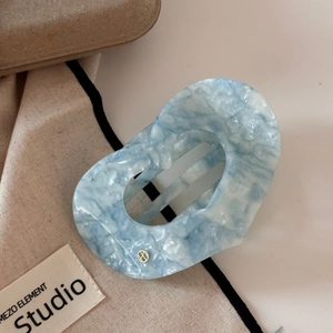 Détail macro d'une pince à cheveux cœur en acétate bleu avec logo en métal doré