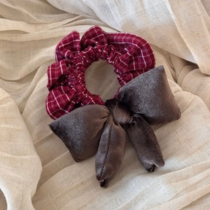 Close-up of red plaid and brown velvet bow hair clip on a soft white fabric background