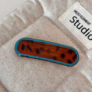 Macro detail of amber tortoiseshell hair clip with contrast blue edge on beige fabric