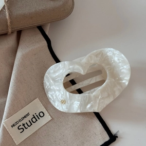 Détail de la pince à cheveux cœur en acétate marbre blanc avec logo doré élégant