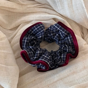 Close-up of navy plaid scrunchie with red velvet trim on soft beige linen fabric