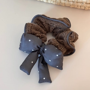 Detail view of a knitted brown scrunchie with a dark grey polka dot bow accessory