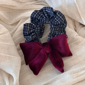 Detail of navy plaid scrunchie with a velvet wine red bow on minimalist fabric background