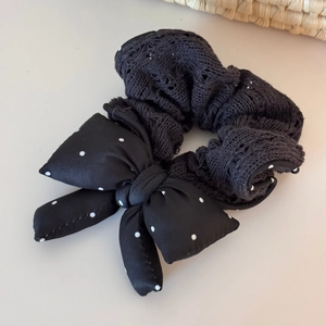 Detailed view of black knit scrunchie with white polka dot bow on cream surface