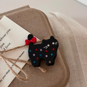 Détail d'une pince à cheveux chat en acétate noir avec strass colorés et petit nœud rouge