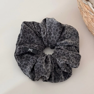Détail d'un chouchou en velours léopard gris montrant la texture et l'étiquette de marque