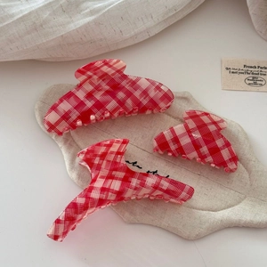 Three red and white checkered acetate hair claw clips on a cream linen background