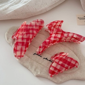 Three sizes of red checkered acetate hair claws displayed on a rustic linen bag