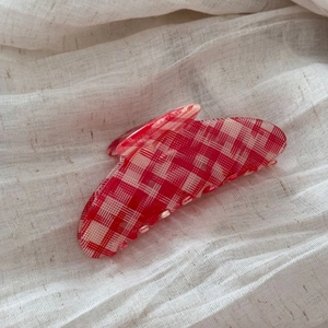 Detail of large red checkered acetate hair claw clip on soft textured linen fabric