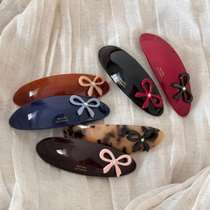 Detailed close-up of six premium acetate hair clips with small crystal bows on silk fabric