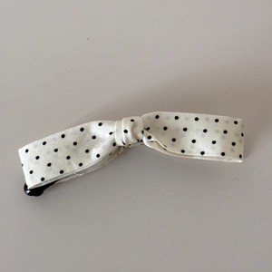 Detail of a large bow hair clip with black polka dots on white satin fabric texture