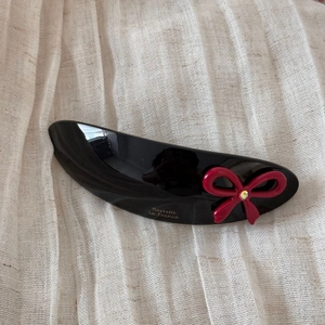 Detail of black acetate hair clip with red bow, rhinestone, and gold Barrette la France text