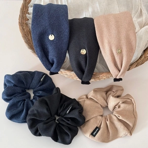 Detail of knitted striped hair scrunchies and headbands with gold logo in a wicker basket
