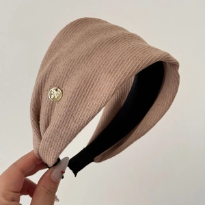 Detail of light brown striped fabric headband with a small gold bow metal emblem