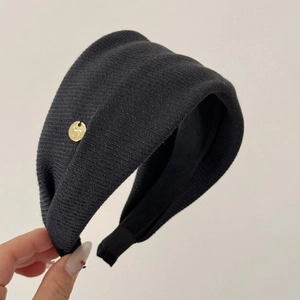 Close-up of black ribbed knit headband featuring a gold round bow metal plaque detail