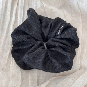 Detail of a large black striped knit hair scrunchie featuring a Hand Made woven label