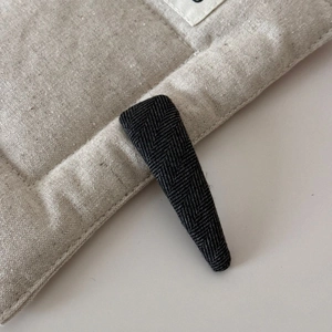Détail d'une pince à cheveux en tissu gris à chevrons sur un fond en lin matelassé