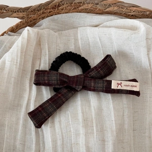 Detail of handmade plaid bow hair clip with white woven label on natural linen background