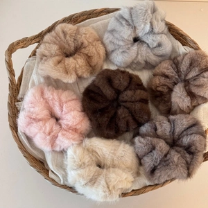 Set of seven fuzzy faux fur scrunchies in neutral autumn colors inside a woven basket