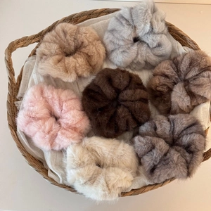 Detailed view of seven plush faux fur scrunchies in various soft colors inside a woven basket