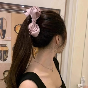 Pink satin bow hair clip styled on a brown ponytail in an elegant indoor setting
